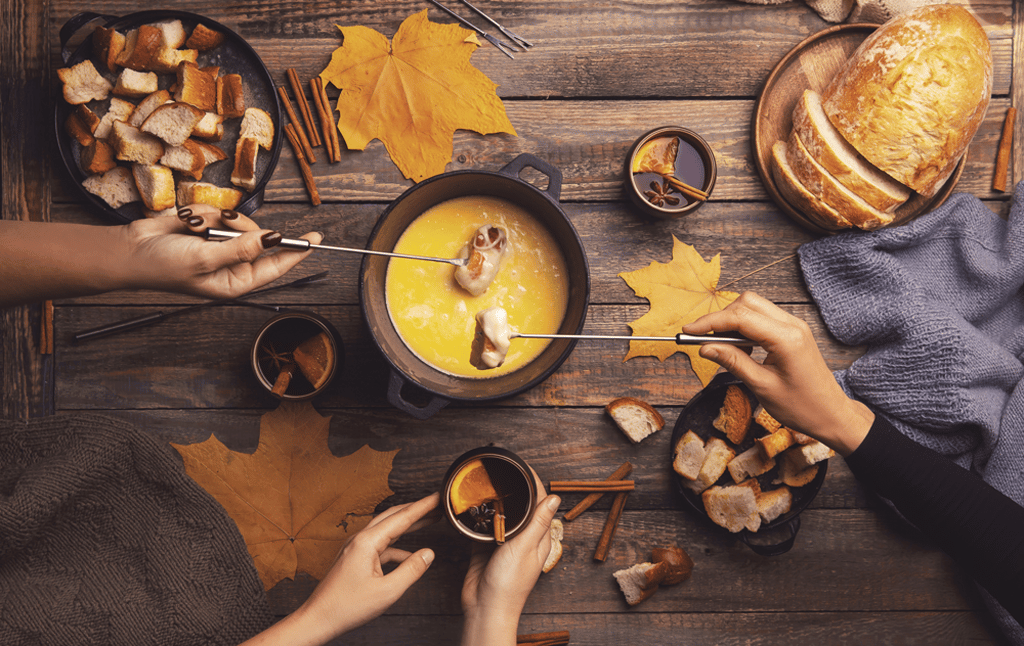 Friends sharing a cheese fondue with bread on a wooden table