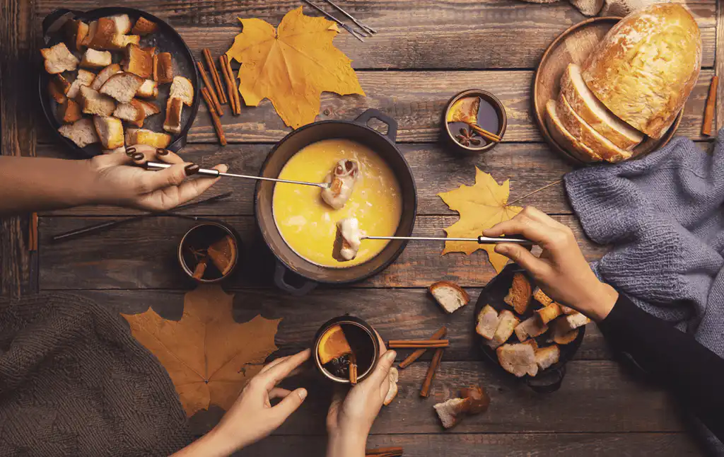 Friends sharing a cheese fondue with bread on a wooden table