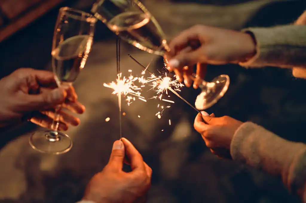 Hands holding sparklers and cheering champagne glasses