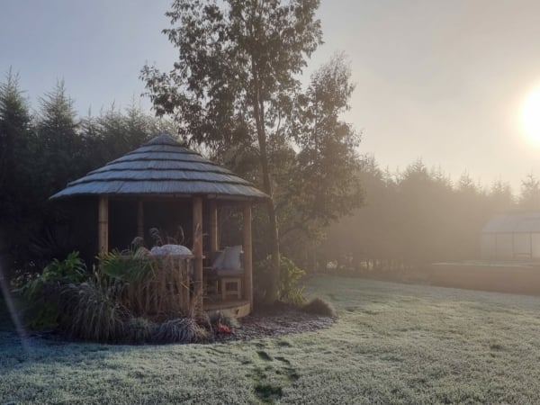 breeze house gazebo with thatched roof in garden covered in frost