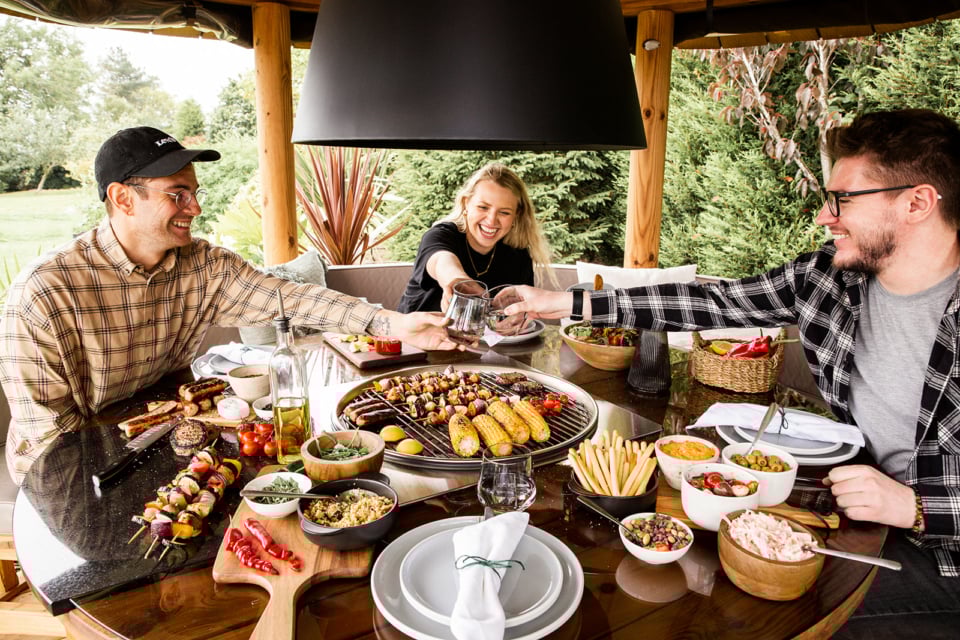 3 people sitting around a table containing BBQ food clinking glasses inside a Breeze House Grill