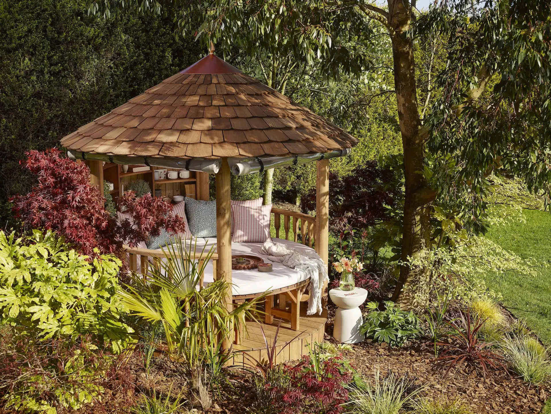 RHS breeze house surrounded by trees and planting in day bed layout featuring sofa seating and coloured cushions