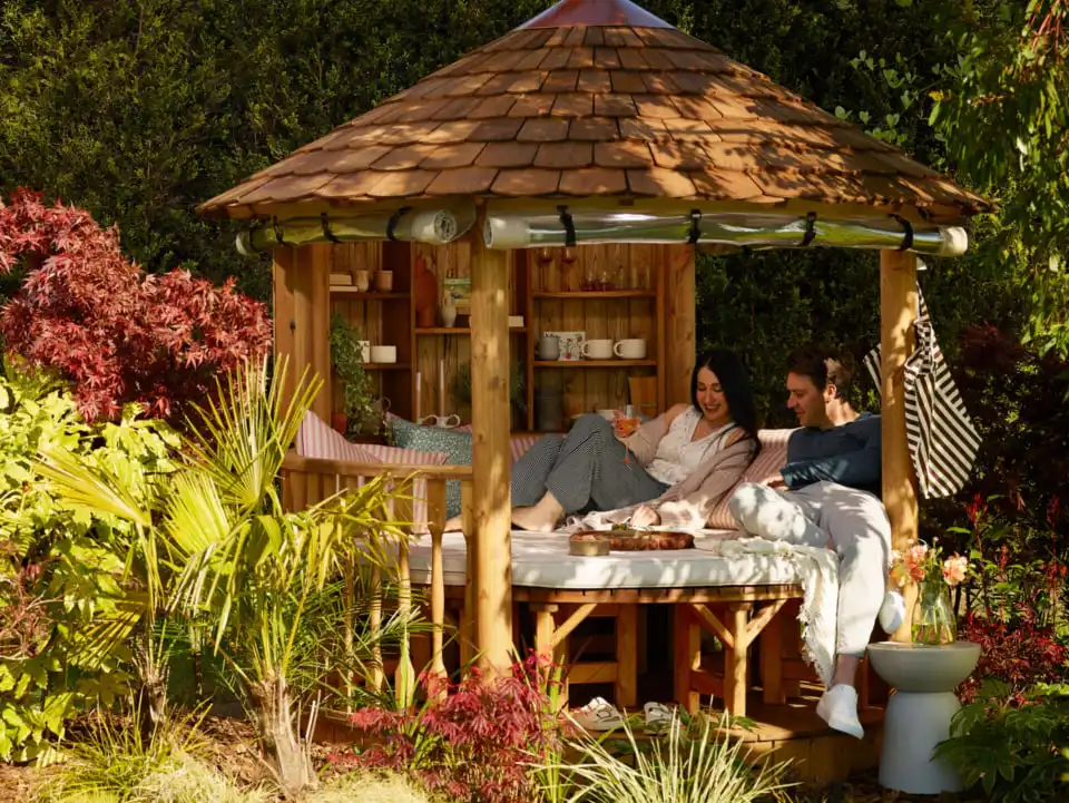 couple sitting inside RHS breeze house in lounge configuration with day bed cushions and blankets