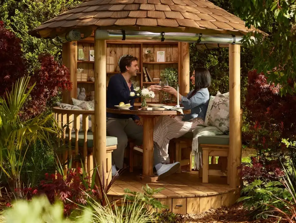 couple sitting inside RHS breeze house with dining configuration raising glasses